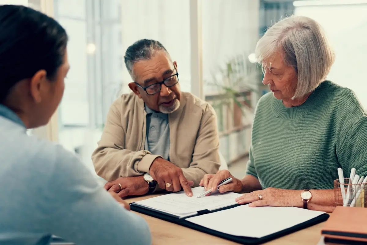 Three people seated at a table reviewing documents together, with one person pointing at a page.